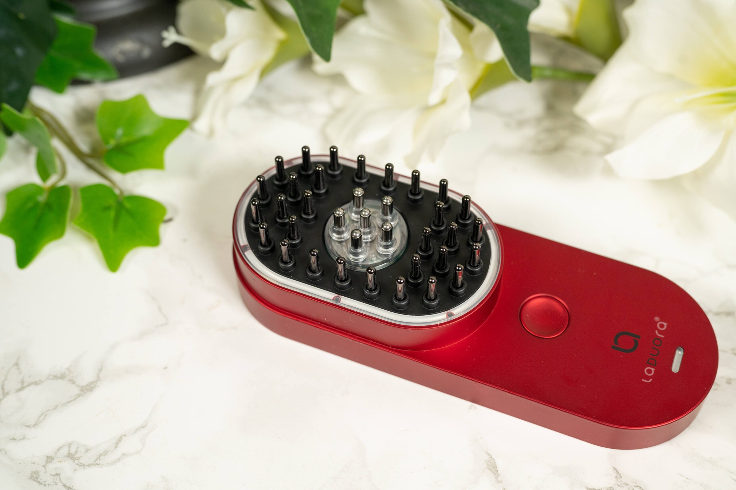 A red Laduora DUO 4 in 1 Scalp and Hair Care Device lying on a marble surface