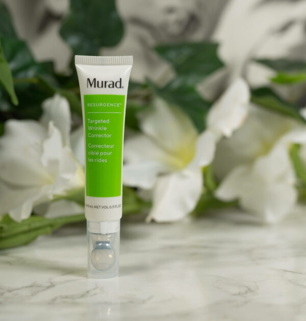 A tube of Murad Resurgence Targeted Wrinkle Corrector standing before white flowers on a dark background