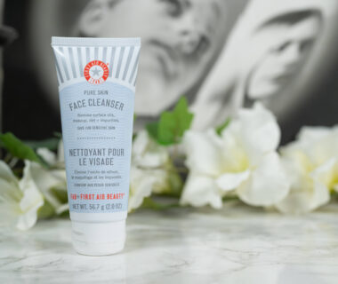 First Aid Beauty Pure Skin Face Cleanser in front of white flowers on a dark background