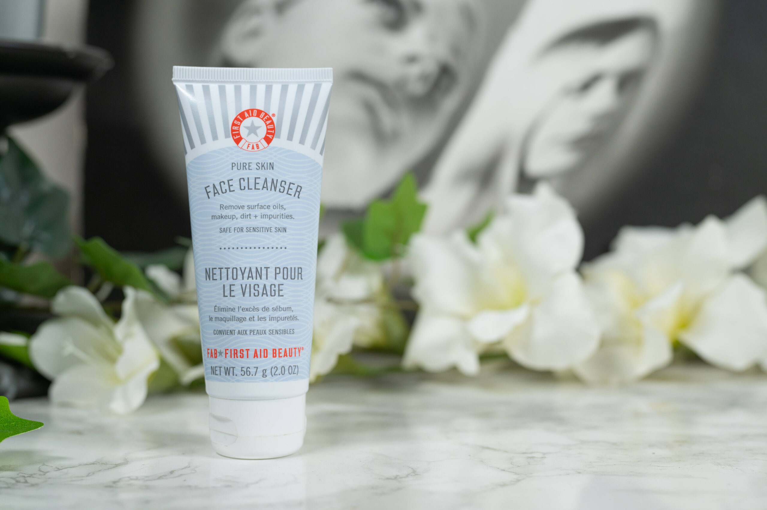 First Aid Beauty Pure Skin Face Cleanser in front of white flowers on a dark background