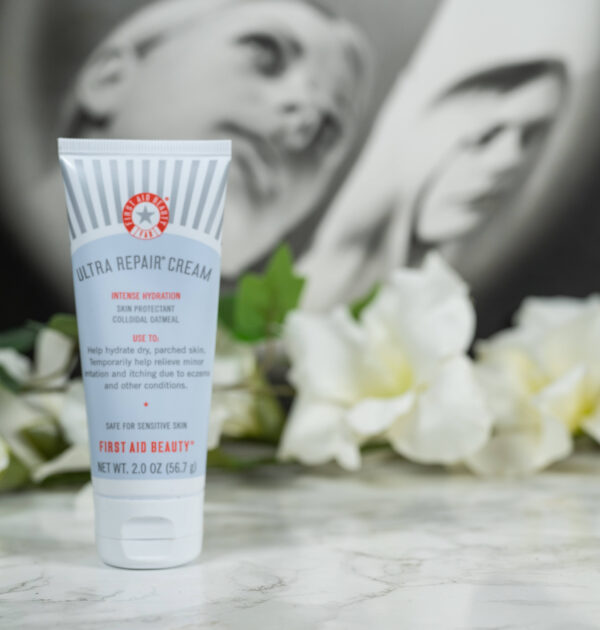 One tube of First Aid Beauty Ultra Repair Cream Intense Hydration in front of white flowers on a dark background