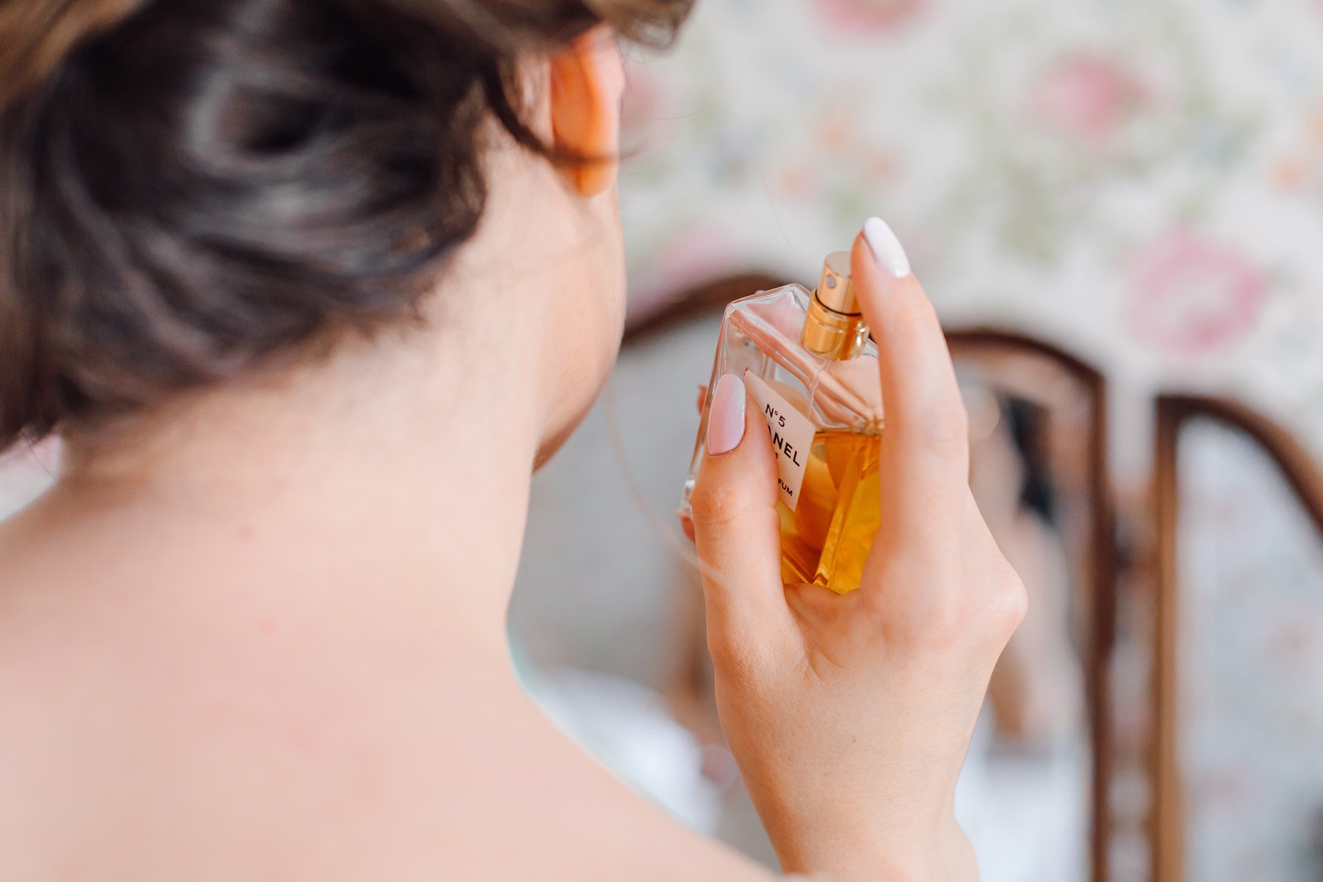 dark haired woman spritzing her exposed neck with a bottle of Chanel No 5