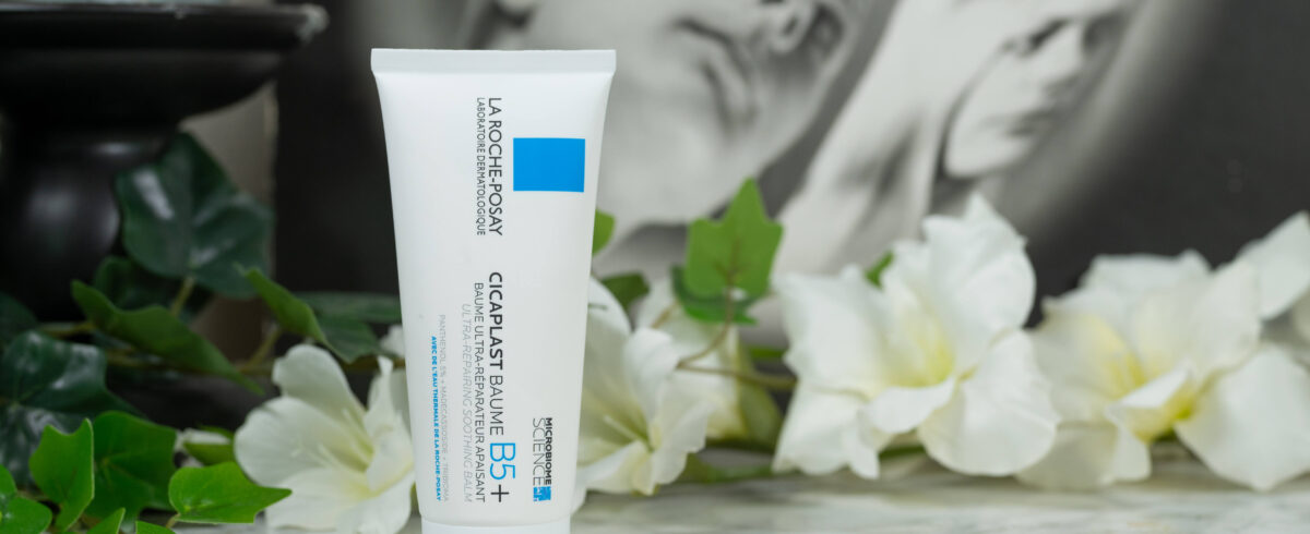 One tube of La Roche Posay Cicaplast Baume B5+ Repairing Cream standing before white flowers on a dark background