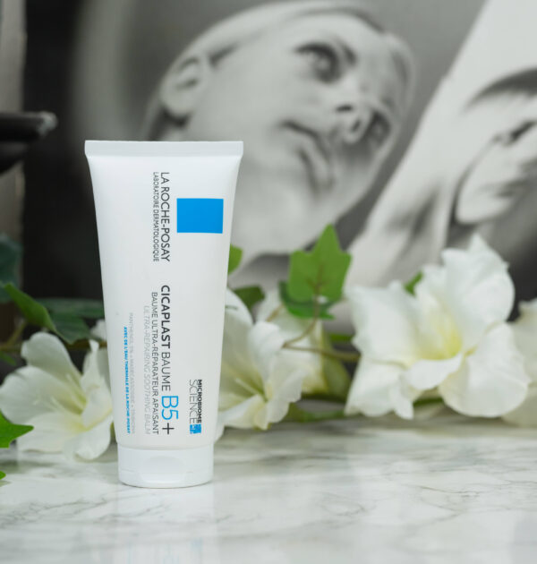 One tube of La Roche Posay Cicaplast Baume B5+ Repairing Cream standing before white flowers on a dark background