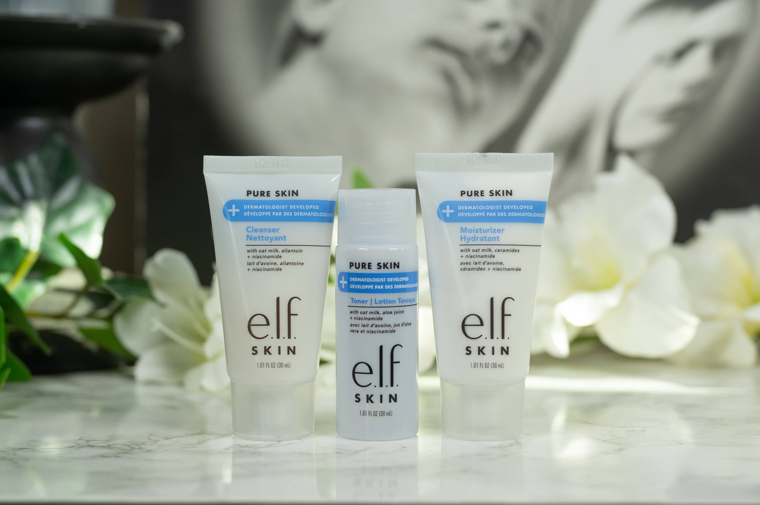 Three products from the e.l.f. skin Pure Skin line standing in front of a dark background with white flowers.