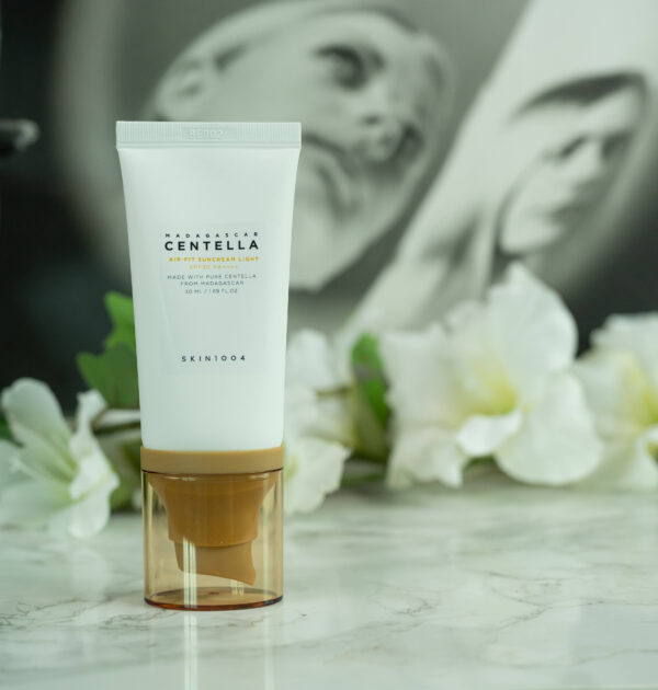 A tube of SKIN1004 Madagascar Centella Air-Fit Suncream Light SPF 30 PA ++++ standing in front of a dark background with white flowers