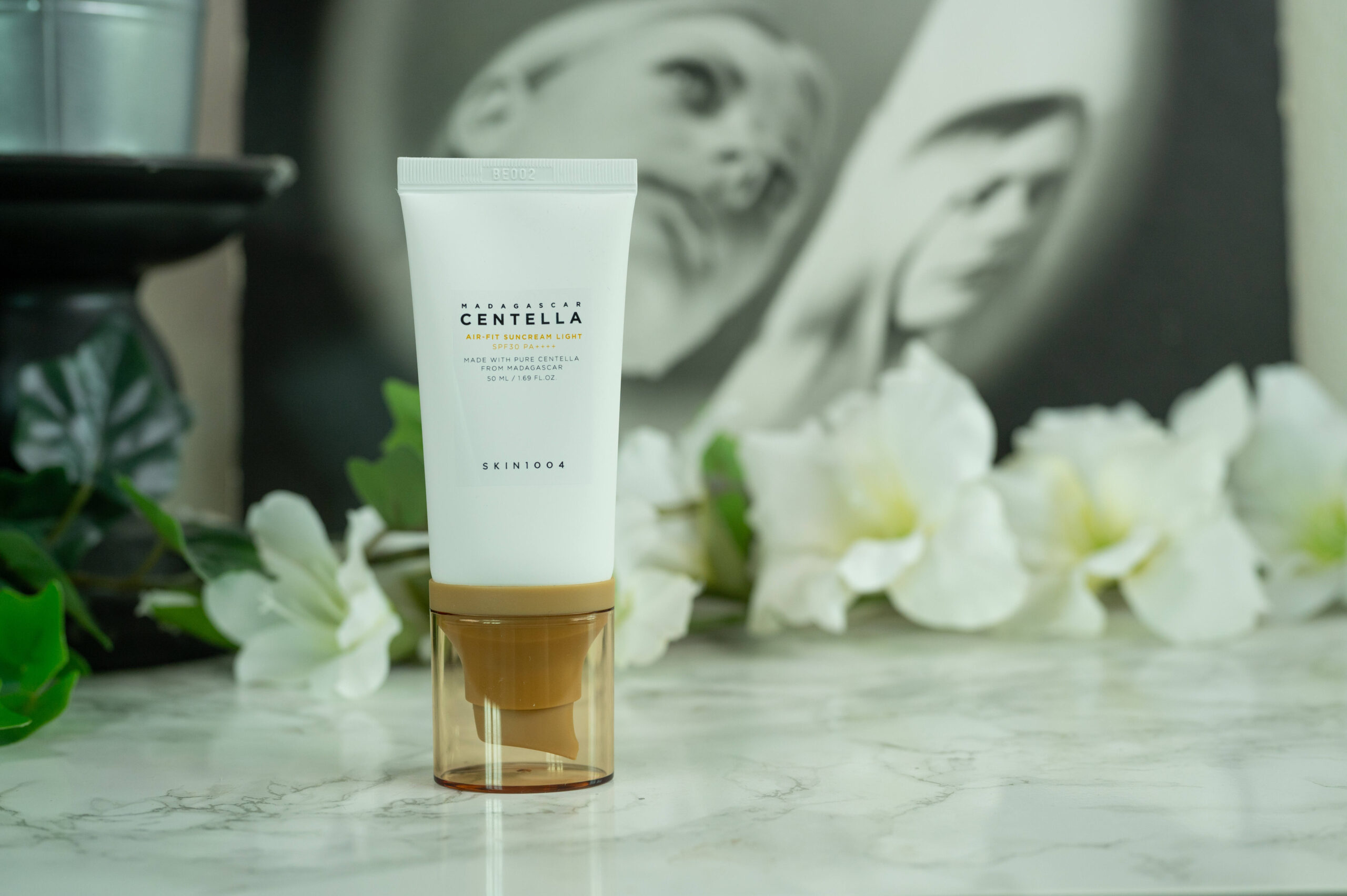 A tube of SKIN1004 Madagascar Centella Air-Fit Suncream Light SPF 30 PA ++++ standing in front of a dark background with white flowers