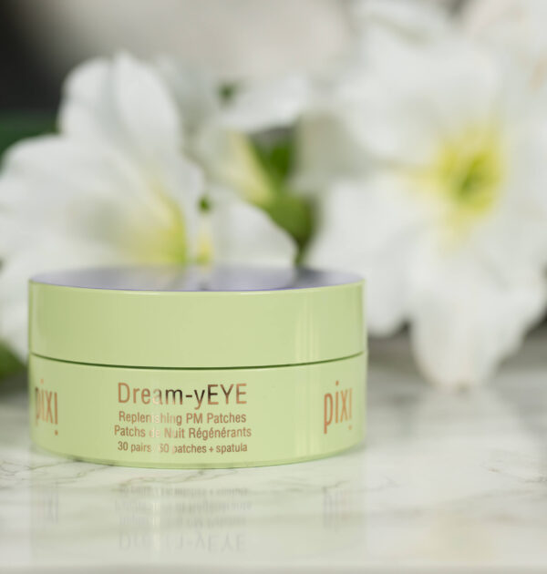 A tube of pixi Dream-yEYE Replenishing PM Patches standing in front of white flowers on a dark background