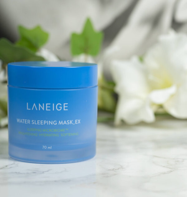 A blue tub of LANEIGE Water Sleeping Mask_EX standing in front of a dark background with white flowers