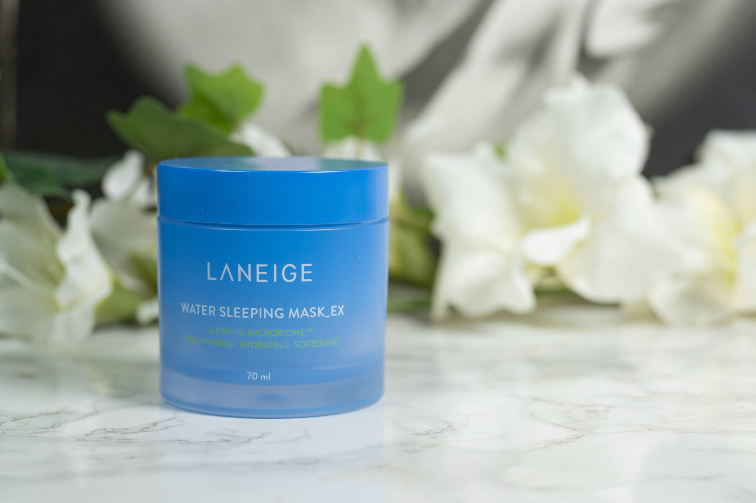 A blue tub of LANEIGE Water Sleeping Mask_EX standing in front of a dark background with white flowers