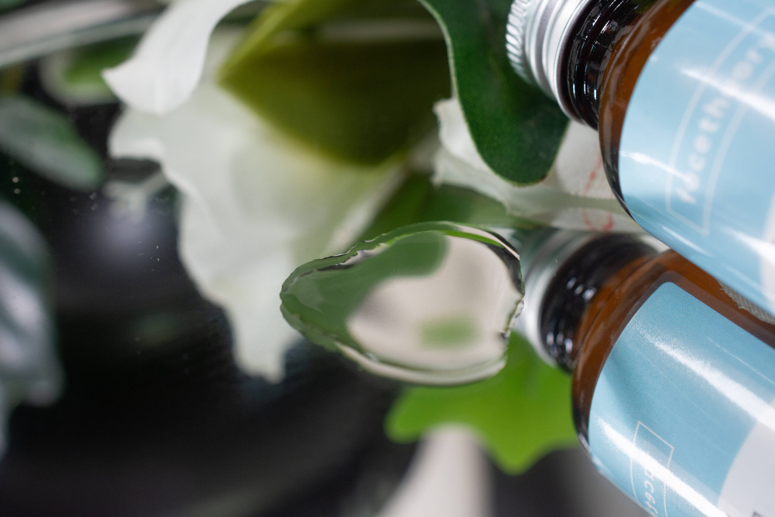 Close up of the facetheory Cera-C Pore Reducing Toner, which looks like water with a slight yellow tint, on a mirrored surface.
