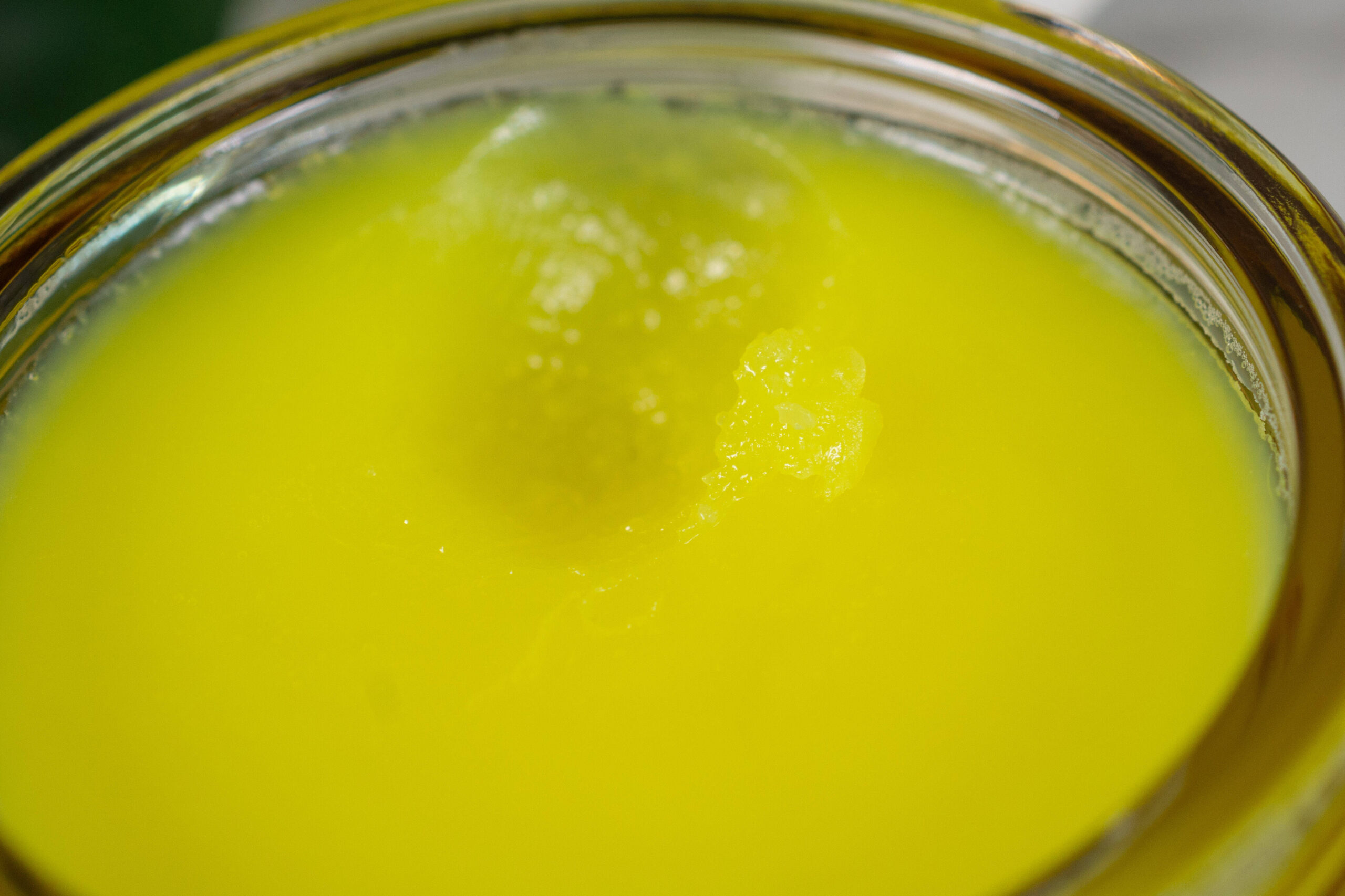 Close up of the True Botanicals Ginger and Turmeric Cleansing Balm, which is neon yellow in the pot