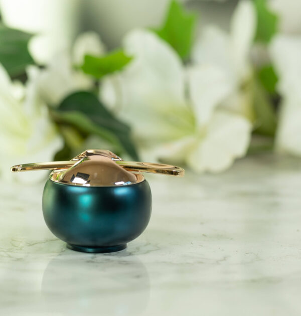 A pot of Florasis Ginseng Care Lip Balm, round and dark teal in color with a golden lid, standing in front of a dark background with white flowers