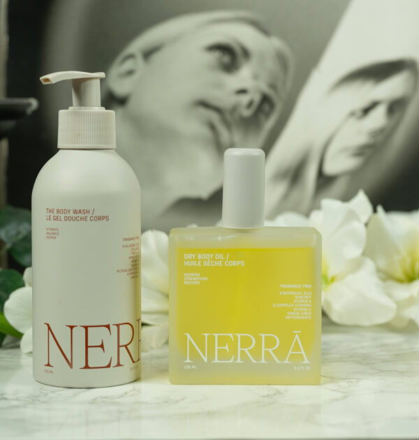 The Nerra Body Care Body Wash and Dry Body Oil standing in front of a dark background with white flowers