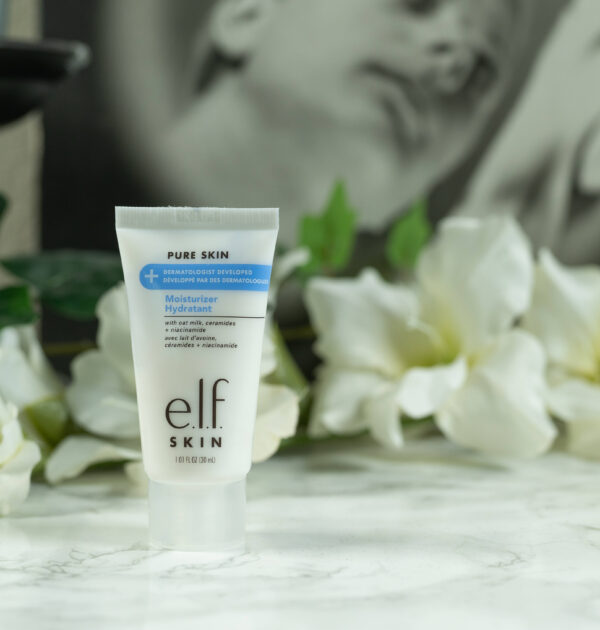 A tube of elf Pure Skin Moisturizer (travel size) standing in front of a dark background with white flowers
