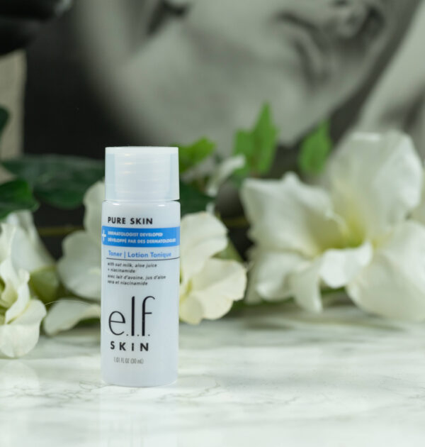 A bottle of e.l.f. Pure Skin Toner (travel size) standing in front of a dark surface with white flowers