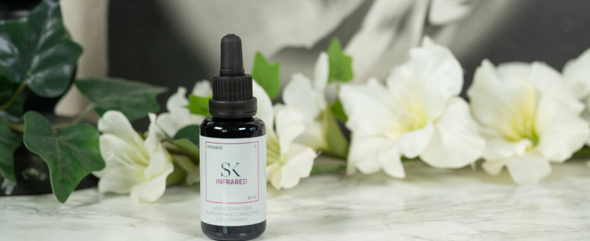 A bottle of Skintegra Infrared Serum standing in front of a dark background with white flowers
