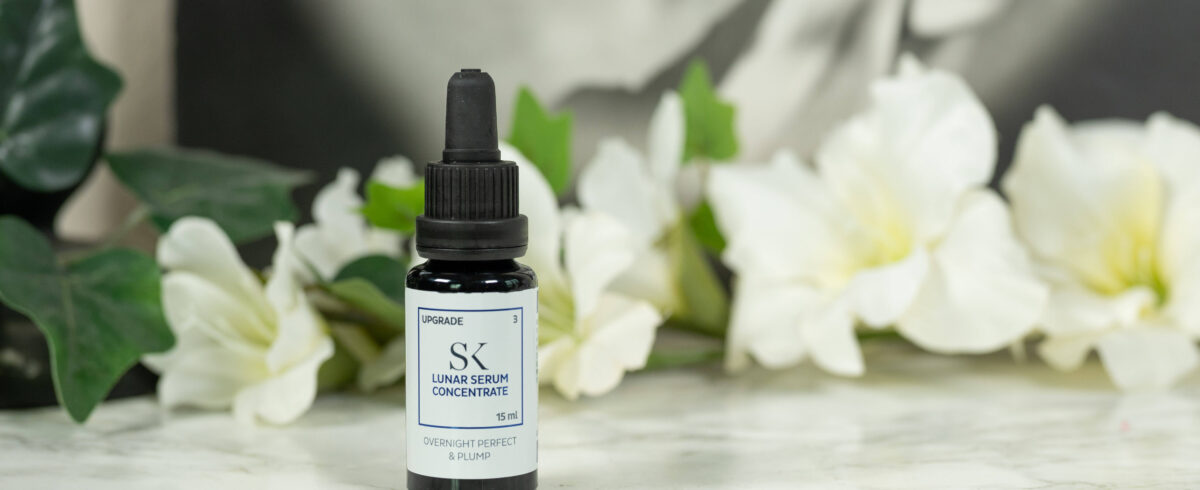 A bottle of Skintegra Lunar Serum Concentrate standing in front of a dark background with white flowers