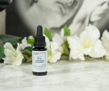 A bottle of Skintegra Lunar Serum Concentrate standing in front of a dark background with white flowers