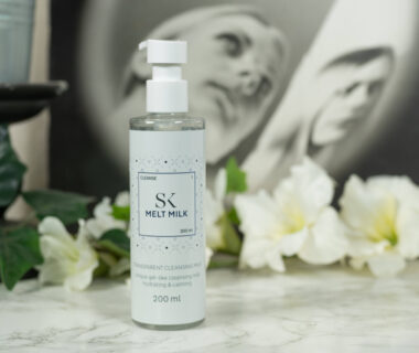 One pump bottle of the Skintegra Melt Milk Cleanser standing in front of a dark background with white flowers