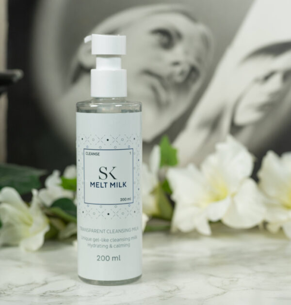 One pump bottle of the Skintegra Melt Milk Cleanser standing in front of a dark background with white flowers