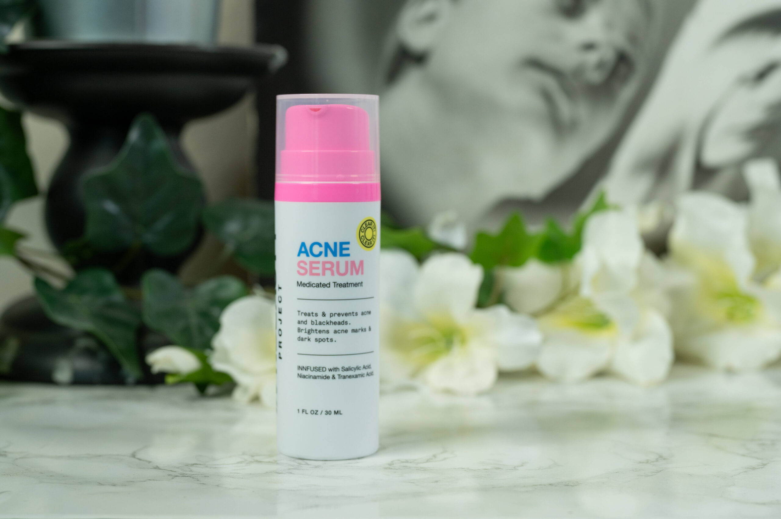 A bottle of innbeauty Project Acne Treatment Review standing in front of a drak background with white flowers