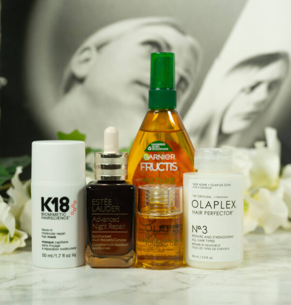 Products from Olaplex, k18, Garnier and Estee Lauder standing in front of a dark background with white flowers
