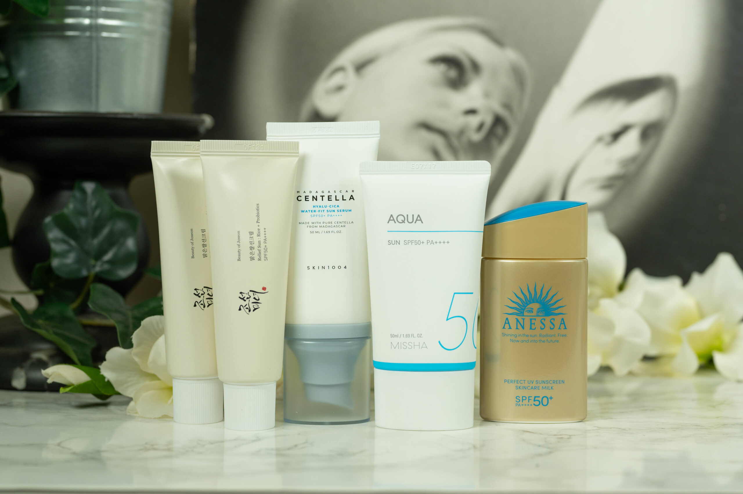 Sunscreens from Beauty of Joseon, SKIN1004, Anessa and MISSHA standing in front of a dark background with white flowers
