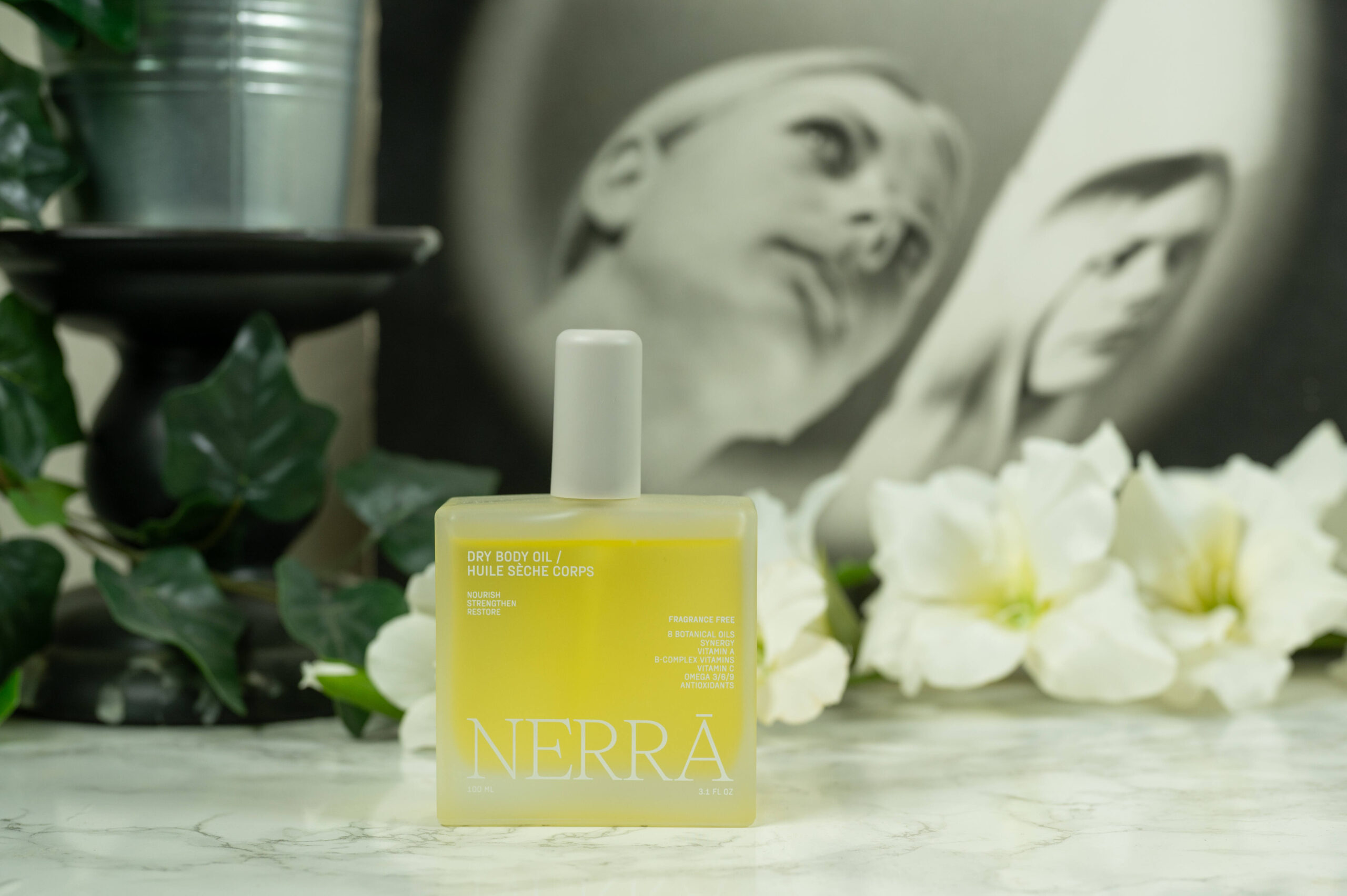 Nerra Dry Body Oil standing in front of a dark background with white flowers