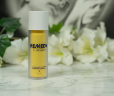 A yellow bottle of Remedy for Dark Spots standing in front of a dark background with white flowers